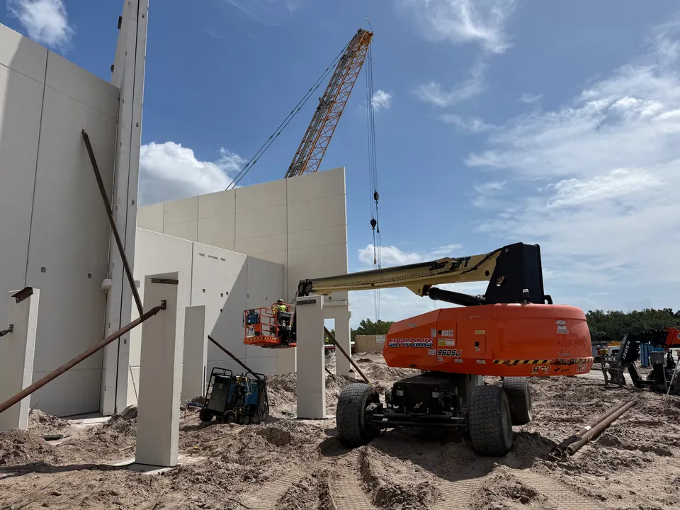 Crane and orange boom lift beside concrete wall panels on a construction site